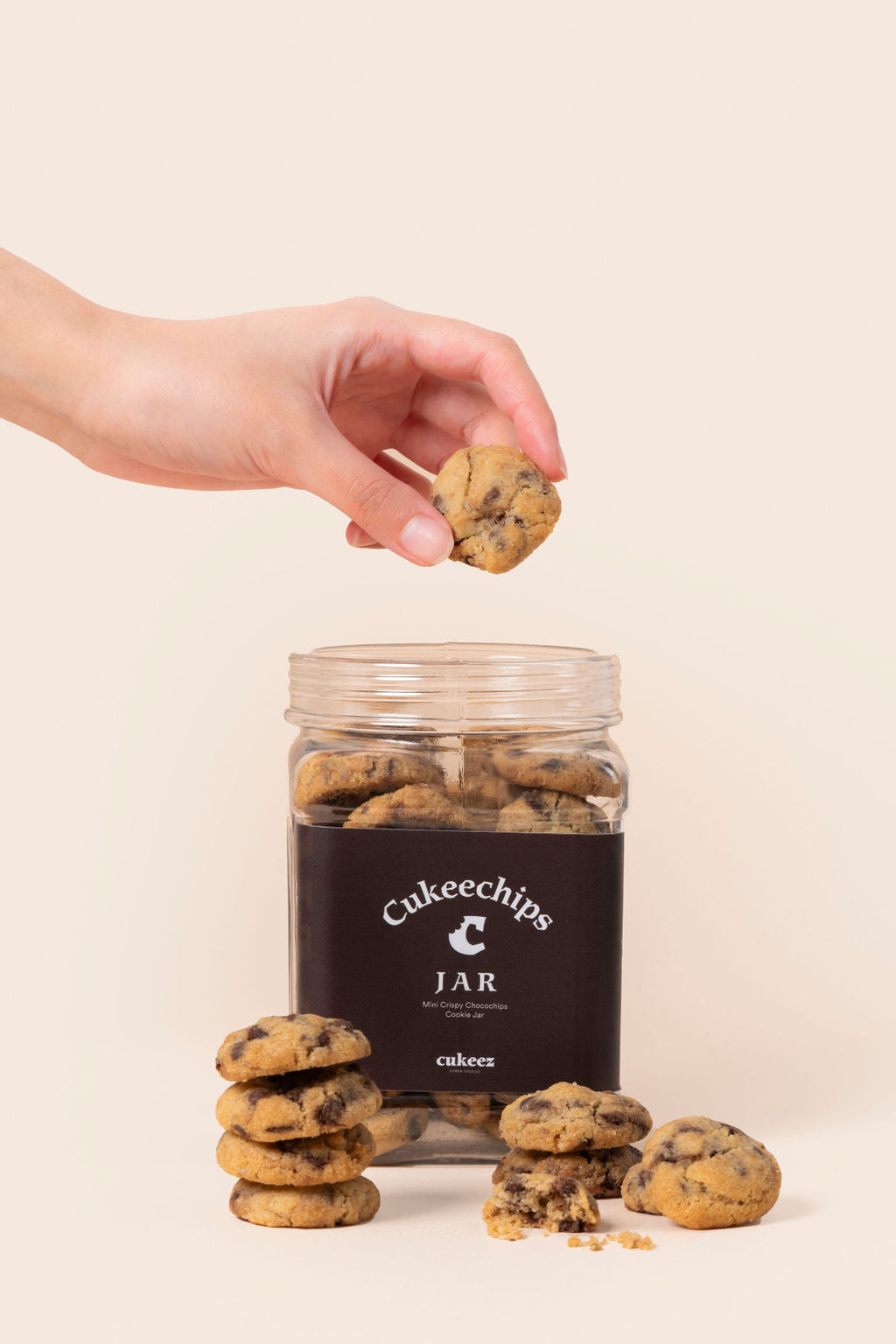 Una mano agarrando una mini cheweez de chocochips y un jar lleno de galletas de chocochips