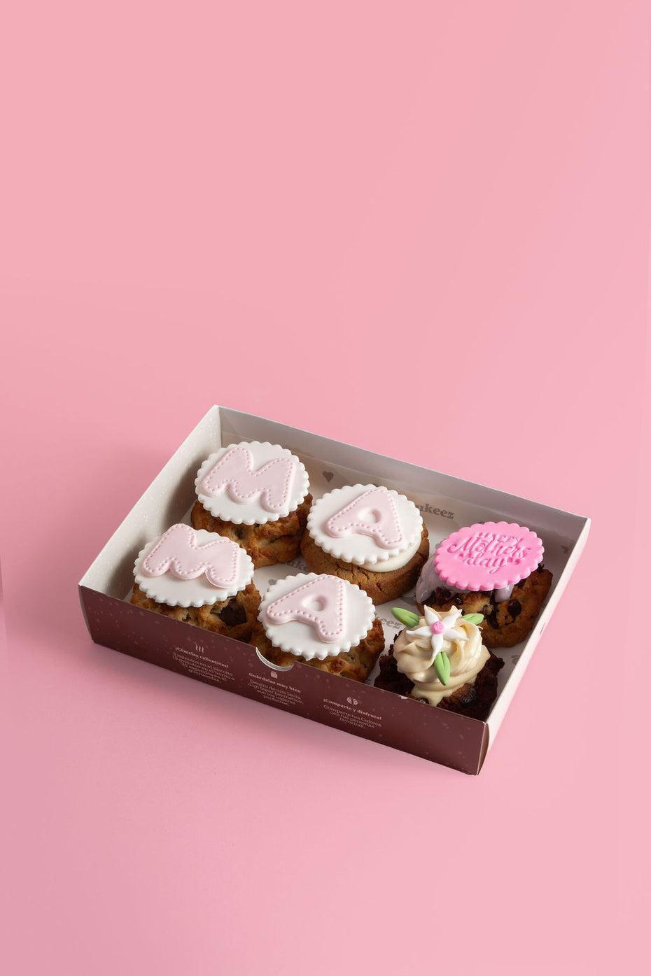 Caja de galletas Cukeez decoradas con fondant blanco y rosa, con letras que forman la palabra “MAMÁ” y diseños especiales como flores y el mensaje “Happy Mother’s Day”, sobre fondo rosa