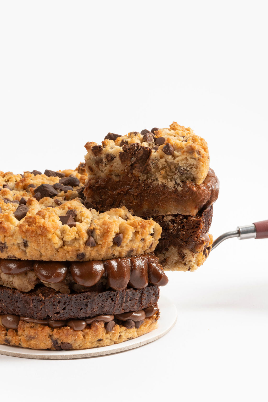 Torta de galleta de dos capas de galleta de vainilla con chips y trozos de chocolate, una capa de nutella, una capa de brownie melcochudo, una capa de cookiedough y una capa de fudge de olla.